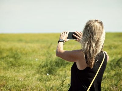 woman in field taking photo with mobile phone